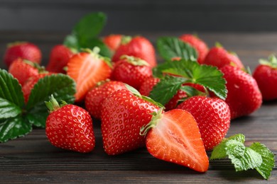 Photo of Fresh ripe strawberries and leaves on black wooden table, closeup