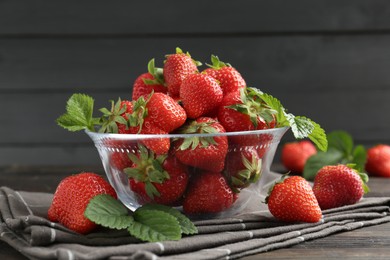 Photo of Fresh ripe strawberries and leaves in container on black wooden table, closeup