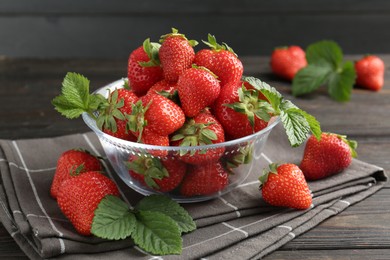 Photo of Fresh ripe strawberries and leaves in container on black wooden table, closeup