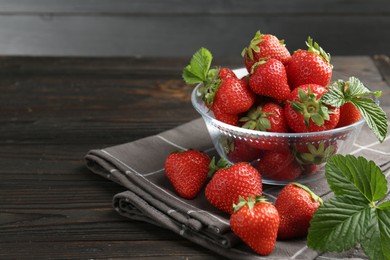 Photo of Fresh ripe strawberries and leaves in container on black wooden table, closeup. Space for text