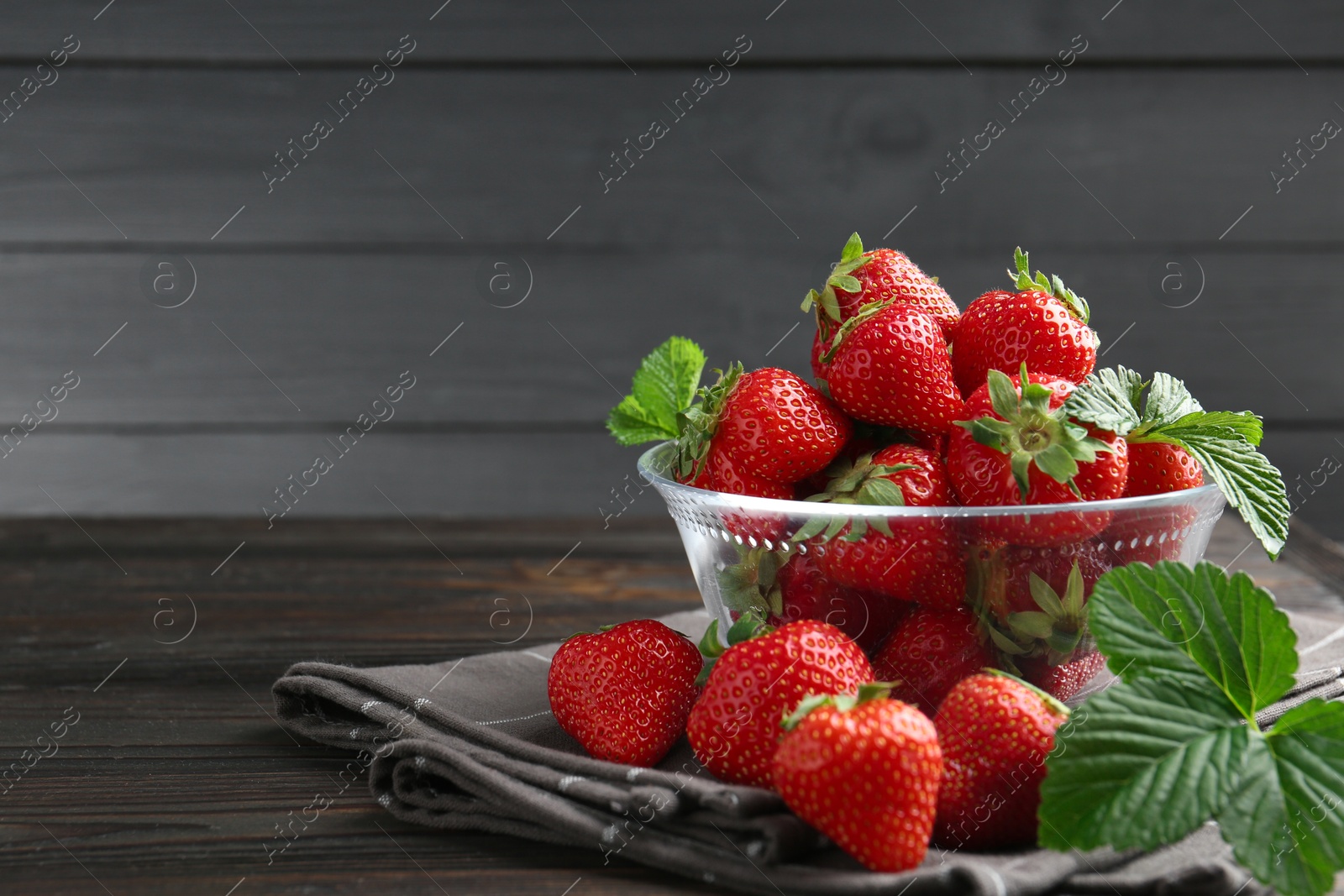 Fresh ripe strawberries and leaves in container on black wooden table, closeup. Space for text Photo of Fresh ripe strawberries and leaves in container on black wooden table, closeup. Space for text