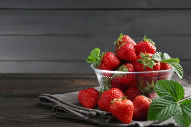 Photo of Fresh ripe strawberries and leaves in container on black wooden table, closeup. Space for text