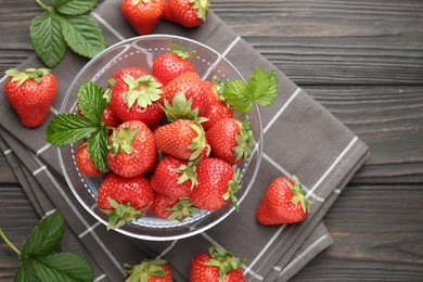 Photo of Fresh ripe strawberries and leaves in container on black wooden table, flat lay. Space for text