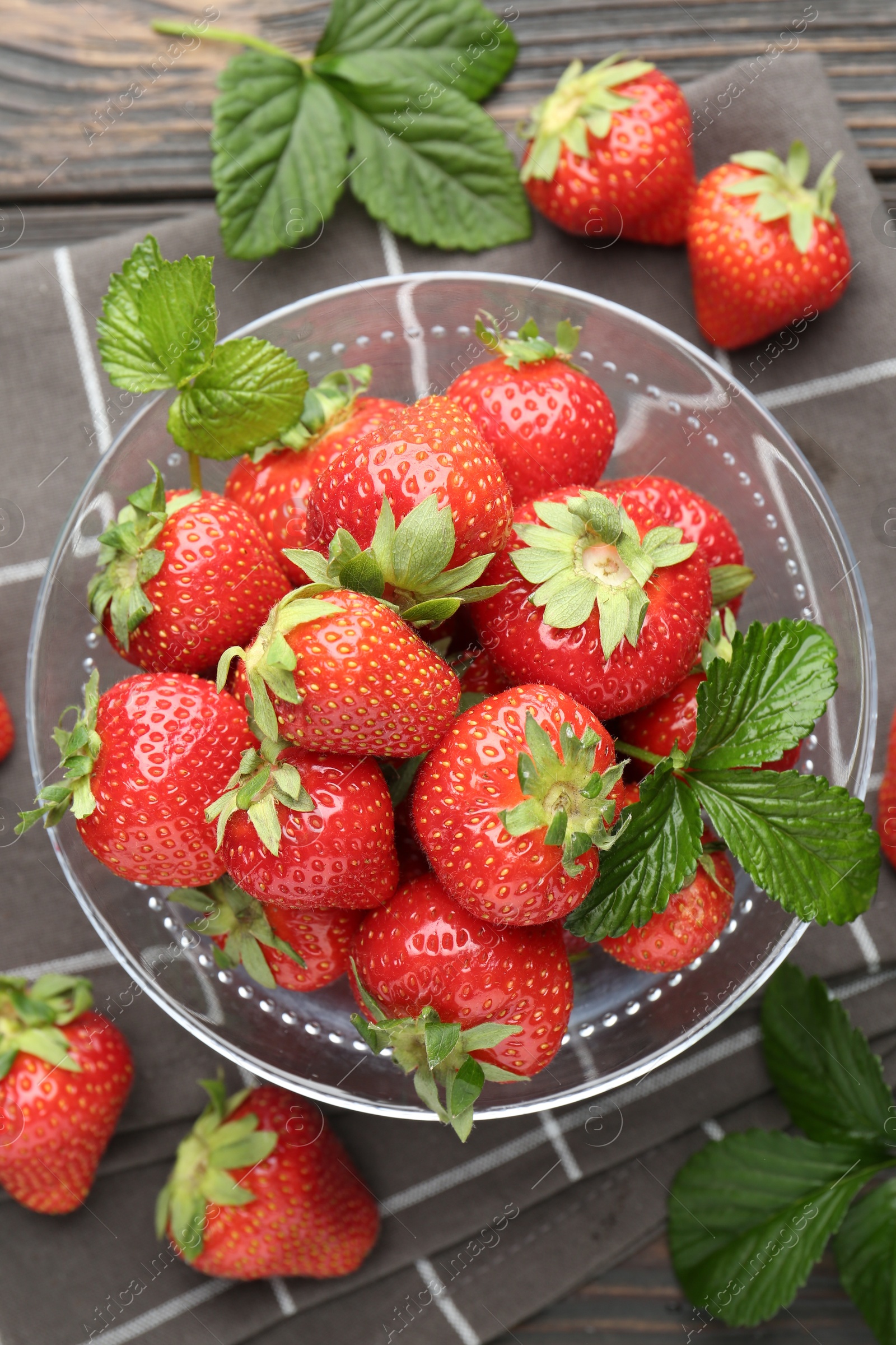 Fresh ripe strawberries and leaves in container on black wooden table, flat lay Photo of Fresh ripe strawberries and leaves in container on black wooden table, flat lay