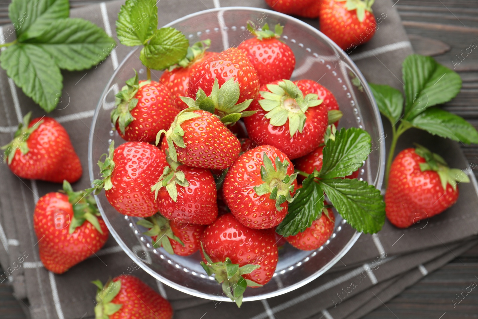 Fresh ripe strawberries and leaves in container on black wooden table, flat lay Photo of Fresh ripe strawberries and leaves in container on black wooden table, flat lay