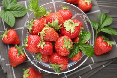 Photo of Fresh ripe strawberries and leaves in container on black wooden table, flat lay