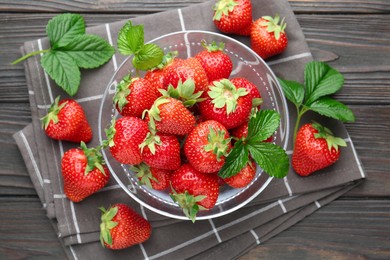 Photo of Fresh ripe strawberries and leaves in container on black wooden table, flat lay