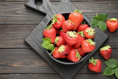 Photo of Fresh ripe strawberries and leaves in bowl on black wooden table, flat lay