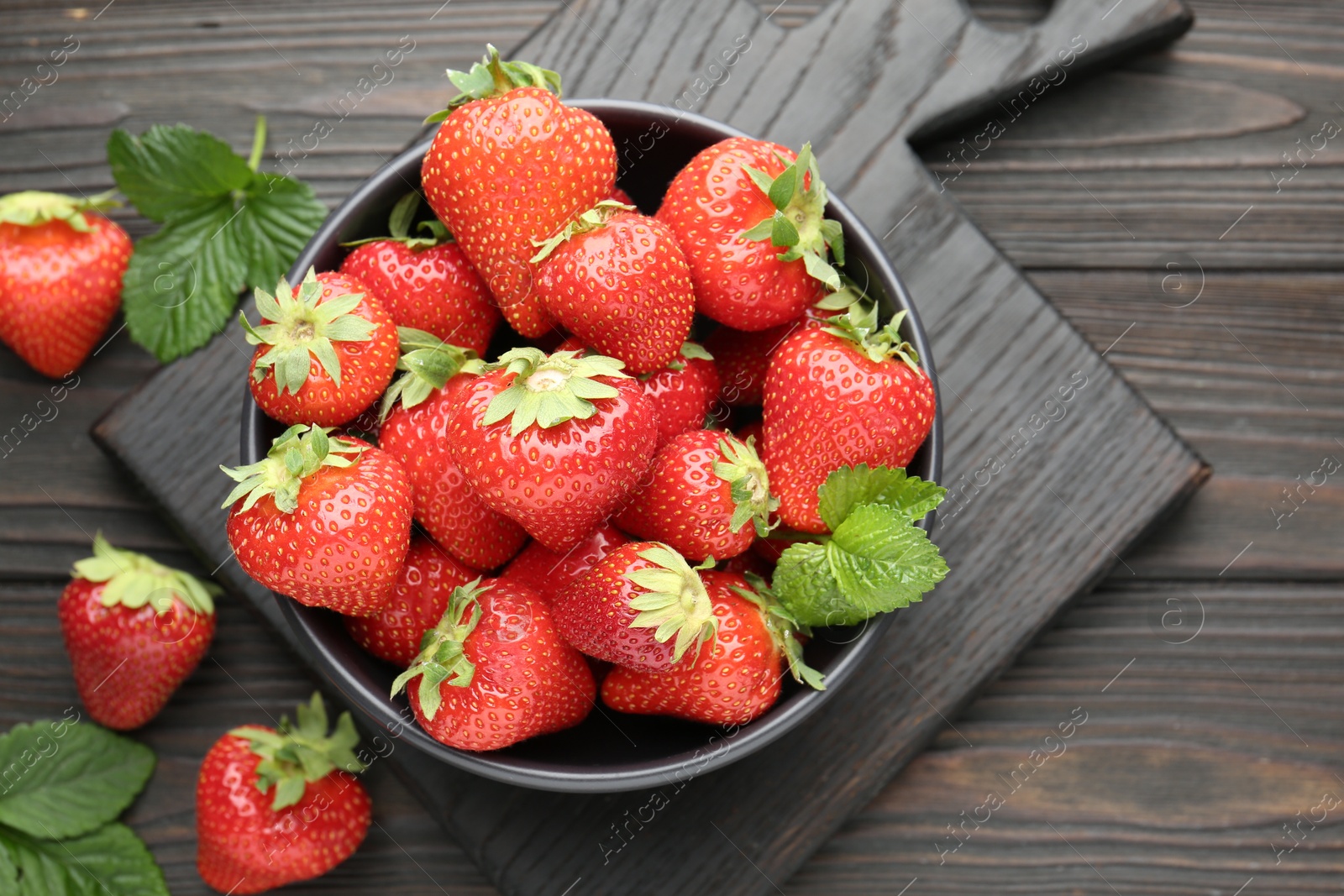 Fresh ripe strawberries and leaves in bowl on black wooden table, flat lay Photo of Fresh ripe strawberries and leaves in bowl on black wooden table, flat lay