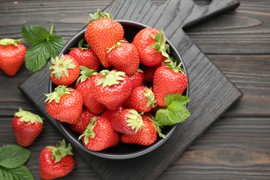 Photo of Fresh ripe strawberries and leaves in bowl on black wooden table, flat lay