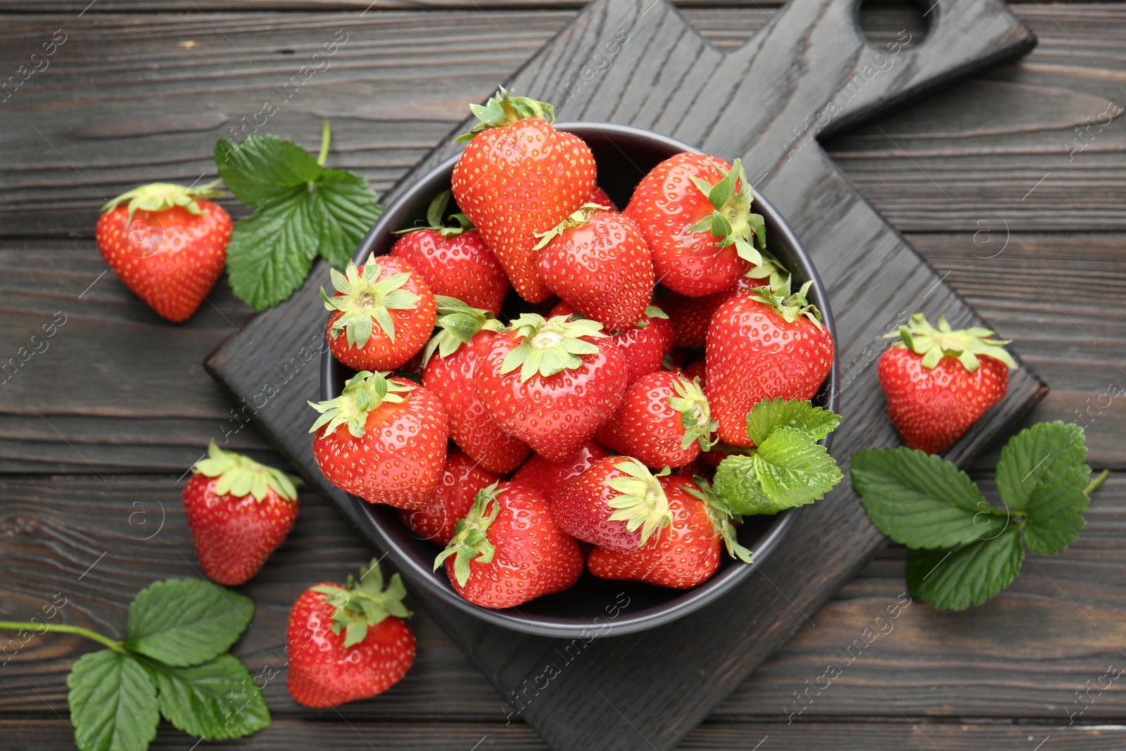 Fresh ripe strawberries and leaves in bowl on black wooden table, flat lay Photo of Fresh ripe strawberries and leaves in bowl on black wooden table, flat lay