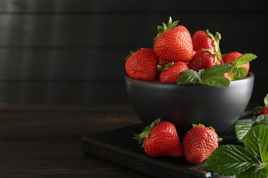Photo of Fresh ripe strawberries and leaves in bowl on black wooden table, closeup. Space for text