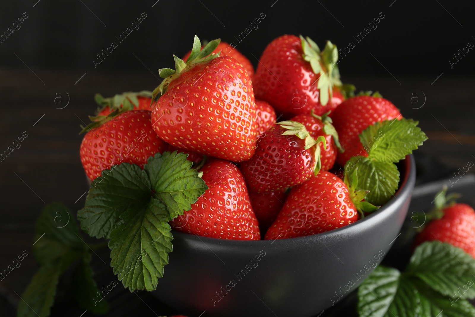 Fresh ripe strawberries and leaves in bowl on black table, closeup Photo of Fresh ripe strawberries and leaves in bowl on black table, closeup