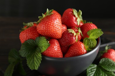 Photo of Fresh ripe strawberries and leaves in bowl on black table, closeup