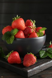 Photo of Fresh ripe strawberries and leaves in bowl on black wooden table, closeup