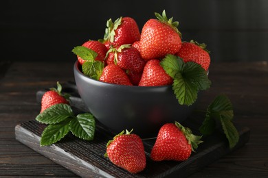 Photo of Fresh ripe strawberries and leaves in bowl on black wooden table, closeup