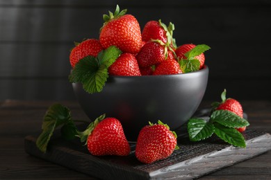 Photo of Fresh ripe strawberries and leaves in bowl on black wooden table, closeup