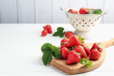 Photo of Fresh ripe strawberries and leaves on white wooden table. Space for text
