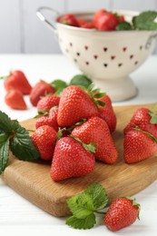 Photo of Fresh ripe strawberries and leaves on white wooden table, closeup