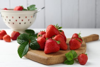 Photo of Fresh ripe strawberries and leaves on white wooden table, closeup
