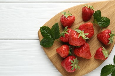 Photo of Fresh ripe strawberries and leaves on white wooden table, top view. Space for text