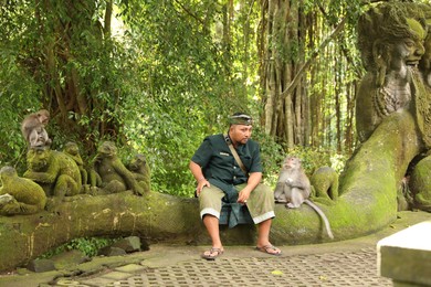 Photo of Bali, Indonesia - June 2, 2025: Man and cute monkeys sitting on ancient statue outdoors