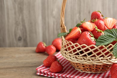 Photo of Delicious ripe strawberries in wicker basket on wooden table, closeup. Space for text