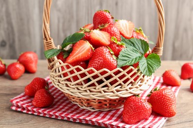 Photo of Delicious ripe strawberries in wicker basket on wooden table, closeup