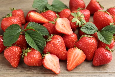 Photo of Delicious ripe strawberries and green leaves on wooden table, closeup
