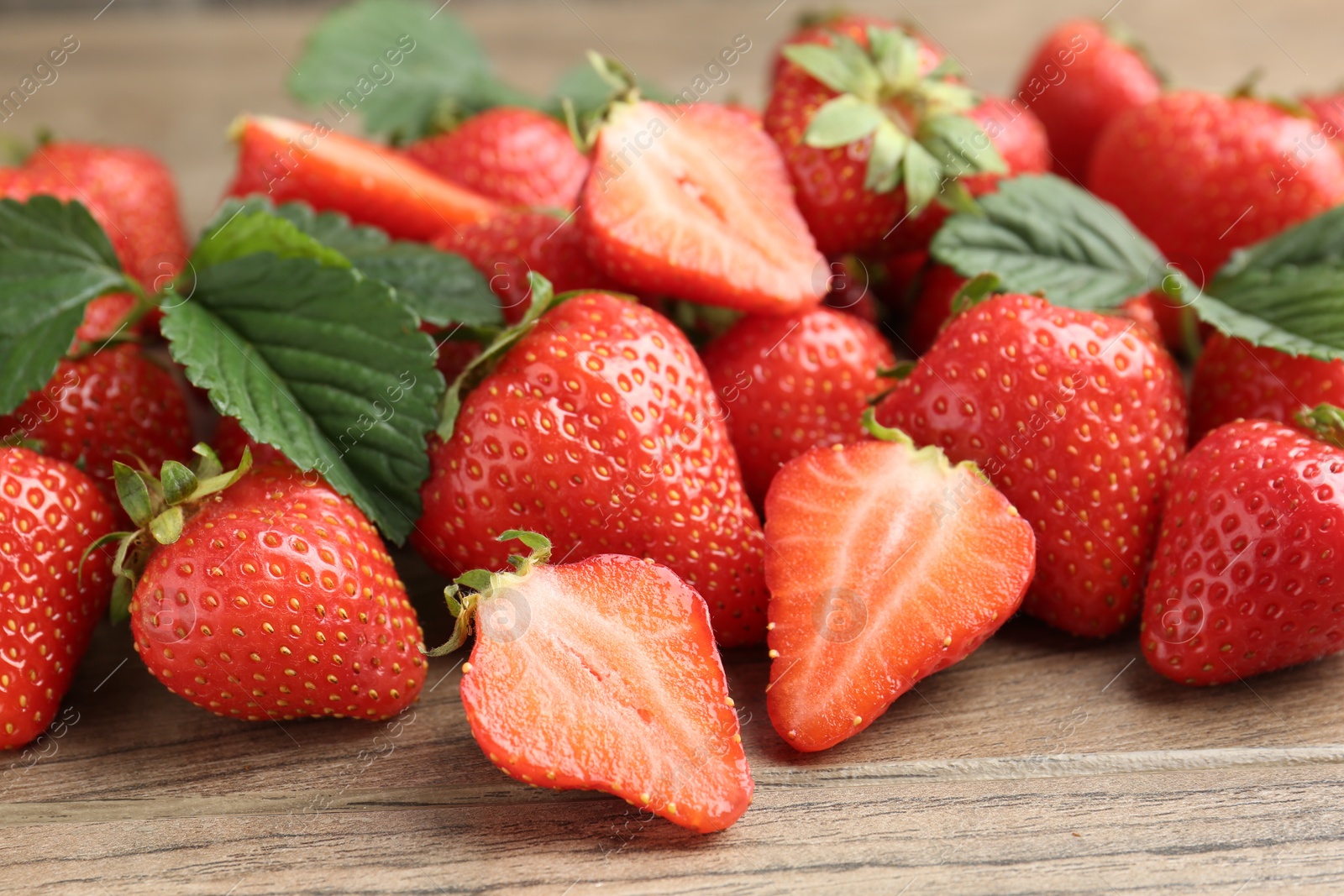 Delicious ripe strawberries and green leaves on wooden table, closeup Photo of Delicious ripe strawberries and green leaves on wooden table, closeup