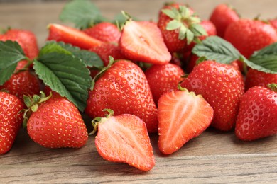 Photo of Delicious ripe strawberries and green leaves on wooden table, closeup