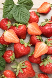 Photo of Delicious ripe strawberries and green leaves on wooden table, flat lay