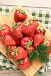 Photo of Delicious ripe strawberries and green leaves on wooden table, top view