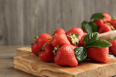 Photo of Delicious ripe strawberries and green leaves on wooden table, closeup