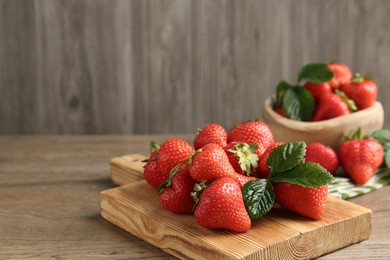 Photo of Delicious ripe strawberries and green leaves on wooden table, closeup. Space for text