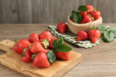 Photo of Delicious ripe strawberries and green leaves on wooden table, closeup. Space for text