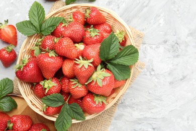 Photo of Delicious ripe strawberries and green leaves on grey table, flat lay. Space for text