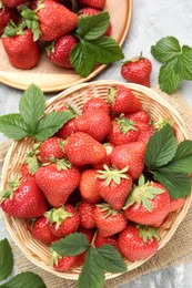 Photo of Delicious ripe strawberries and green leaves on grey table, flat lay