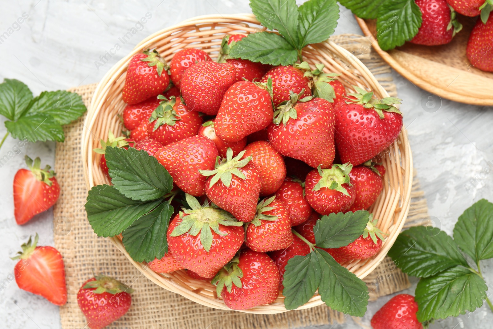 Delicious ripe strawberries and green leaves on grey table, flat lay Photo of Delicious ripe strawberries and green leaves on grey table, flat lay