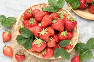 Photo of Delicious ripe strawberries and green leaves on grey table, flat lay
