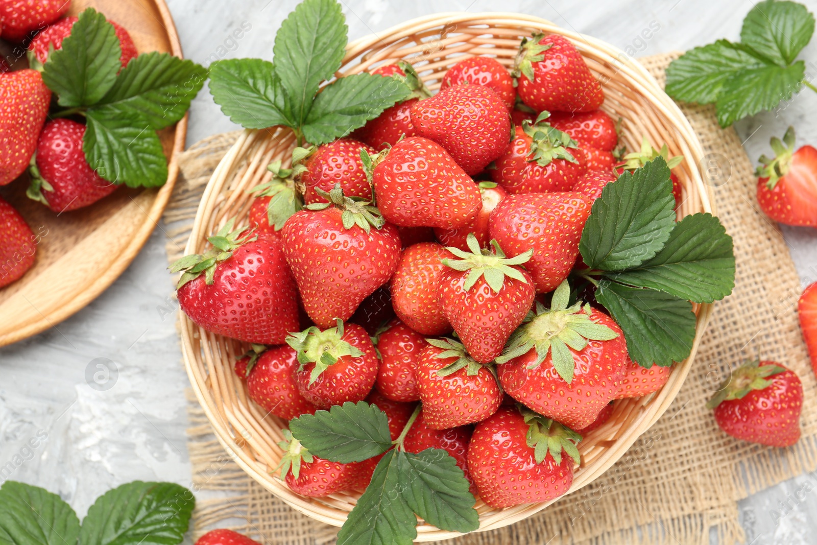 Delicious ripe strawberries and green leaves on grey table, flat lay Photo of Delicious ripe strawberries and green leaves on grey table, flat lay