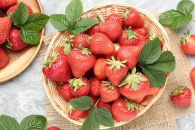 Photo of Delicious ripe strawberries and green leaves on grey table, flat lay