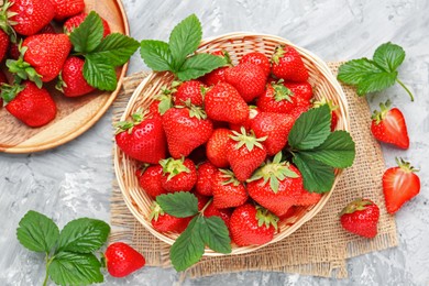 Photo of Delicious ripe strawberries and green leaves on grey table, flat lay