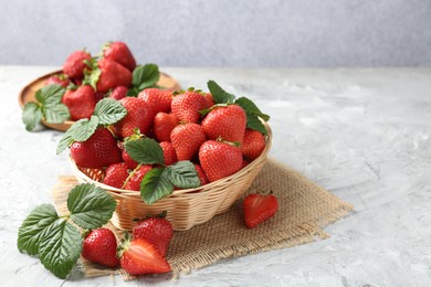 Photo of Delicious ripe strawberries and green leaves on grey table, closeup. Space for text