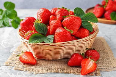 Photo of Delicious ripe strawberries and green leaves on grey table, closeup