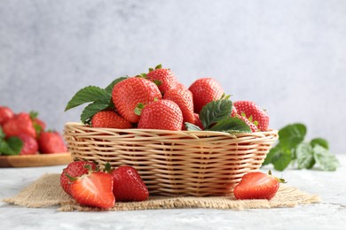Photo of Delicious ripe strawberries and green leaves on grey table, closeup