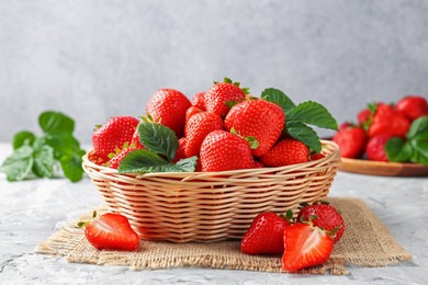 Photo of Delicious ripe strawberries and green leaves on grey table, closeup