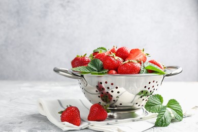 Photo of Delicious ripe strawberries and green leaves on grey table, closeup. Space for text