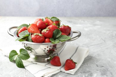 Photo of Delicious ripe strawberries and green leaves on grey table, closeup. Space for text