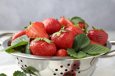 Photo of Delicious ripe strawberries and green leaves in colander on table, closeup